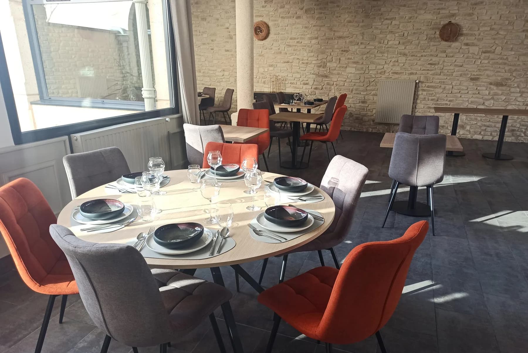 La salle du restaurant : murs en pierre, fauteuils terracotta et lumière naturelle